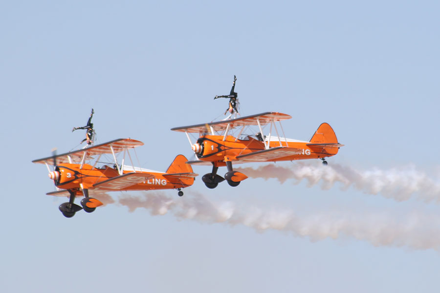 2 orange bi-planes in an air show with stunt people on top