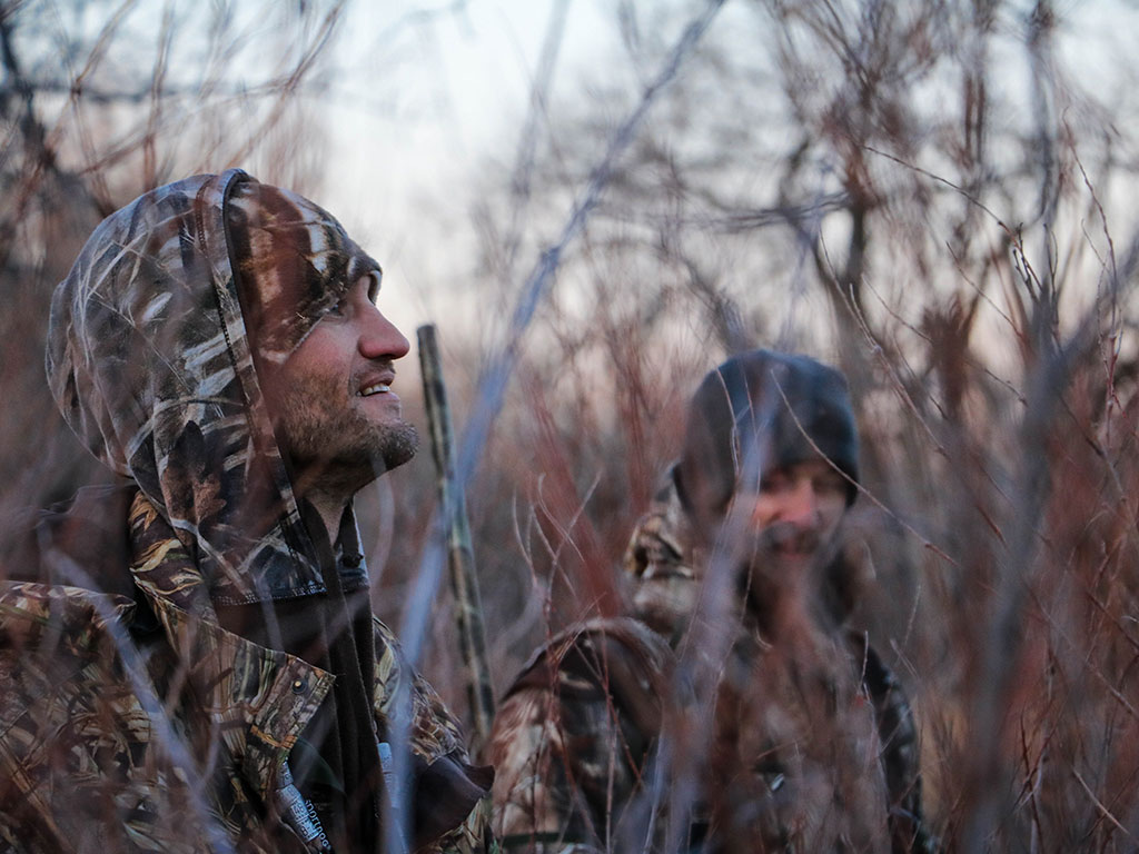 two hunters with their shotguns sitting in a marsh duck hunting